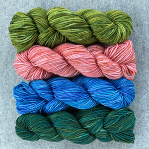 A photo of 4 skeins of yarn that make up the Painted Hive collection. From top to bottom:  grassy meadow (green), jester's blush (pink), angel blue and devil green. 